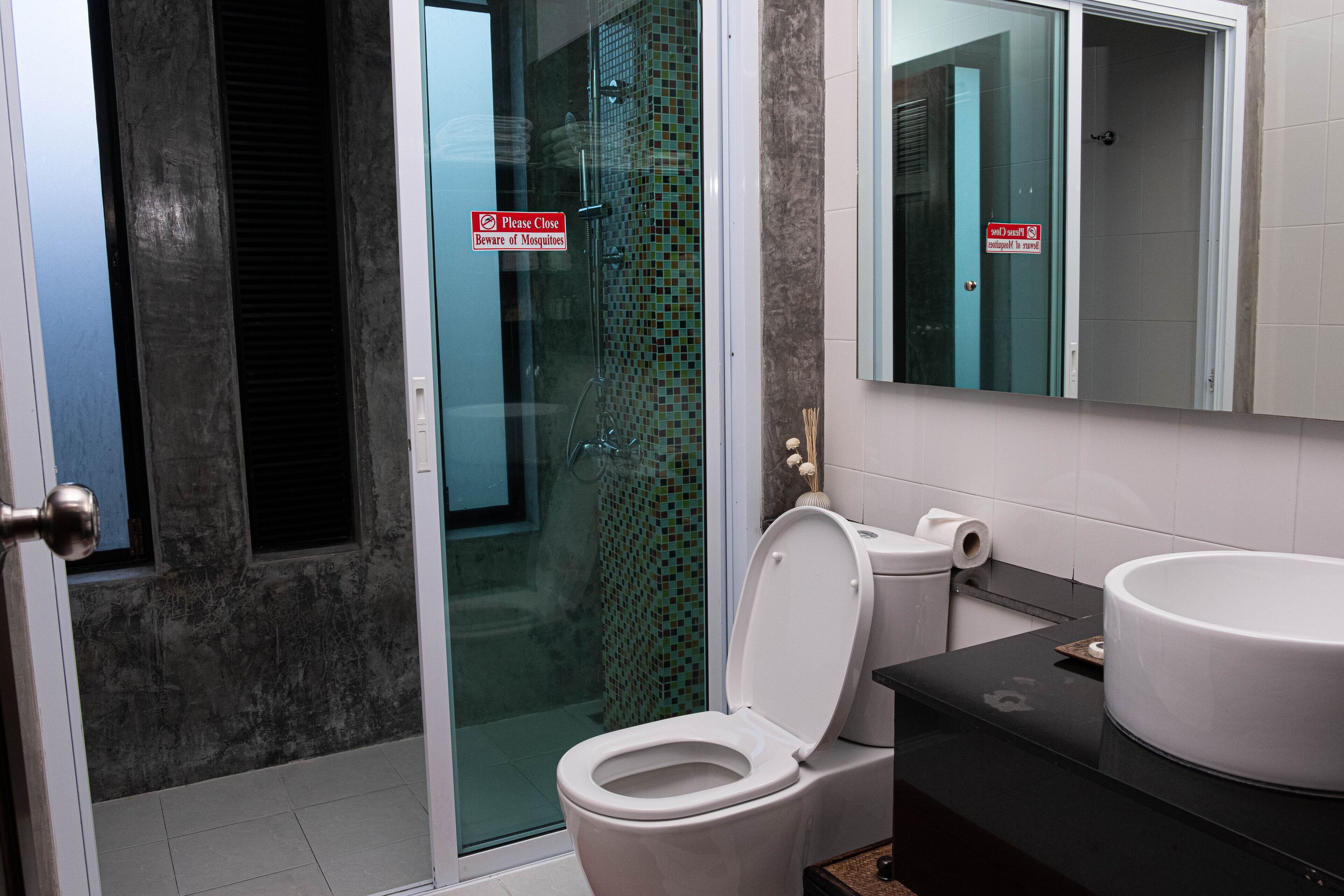 A bathroom with a glass shower door, a toilet with a closed lid, and a sink with a mirror above it.