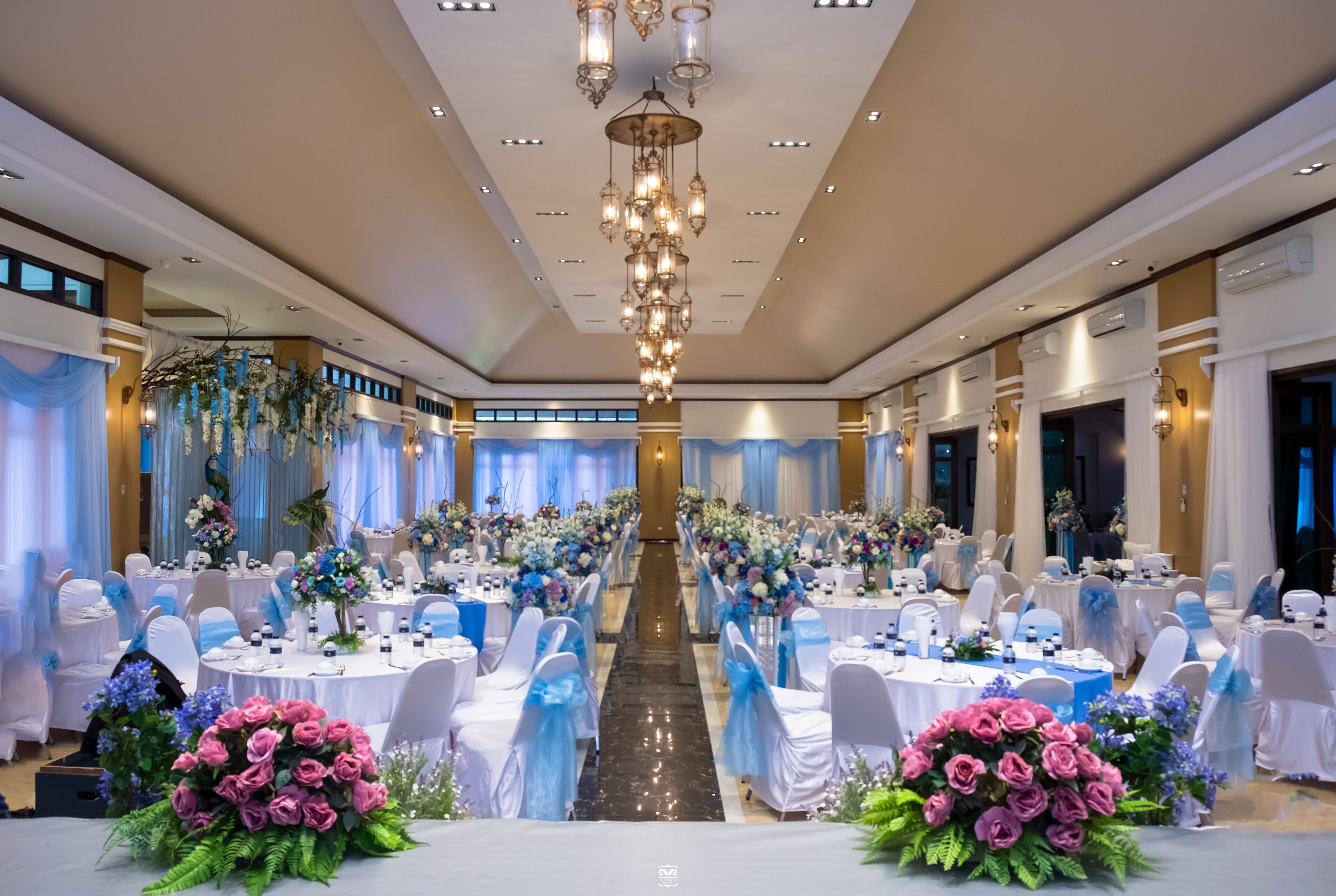 A banquet hall with round tables, white chairs, and floral centerpieces.