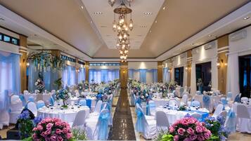 A banquet hall with round tables, white chairs, and floral centerpieces.