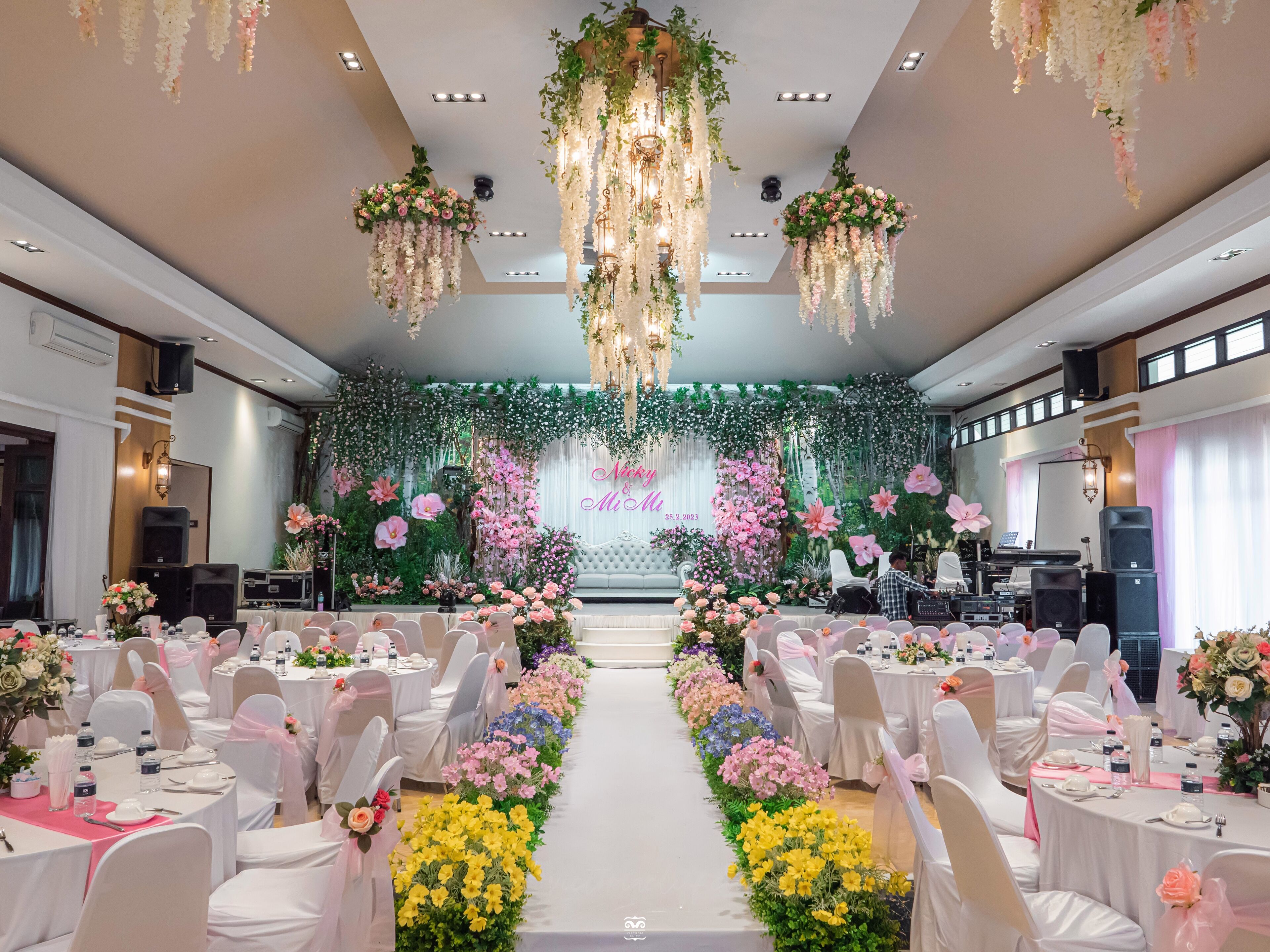 A banquet hall with round tables, white chairs, and floral centerpieces.