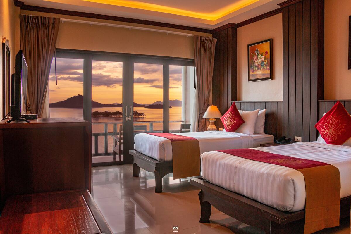 A hotel room with two beds, a desk, and a view of the sea.