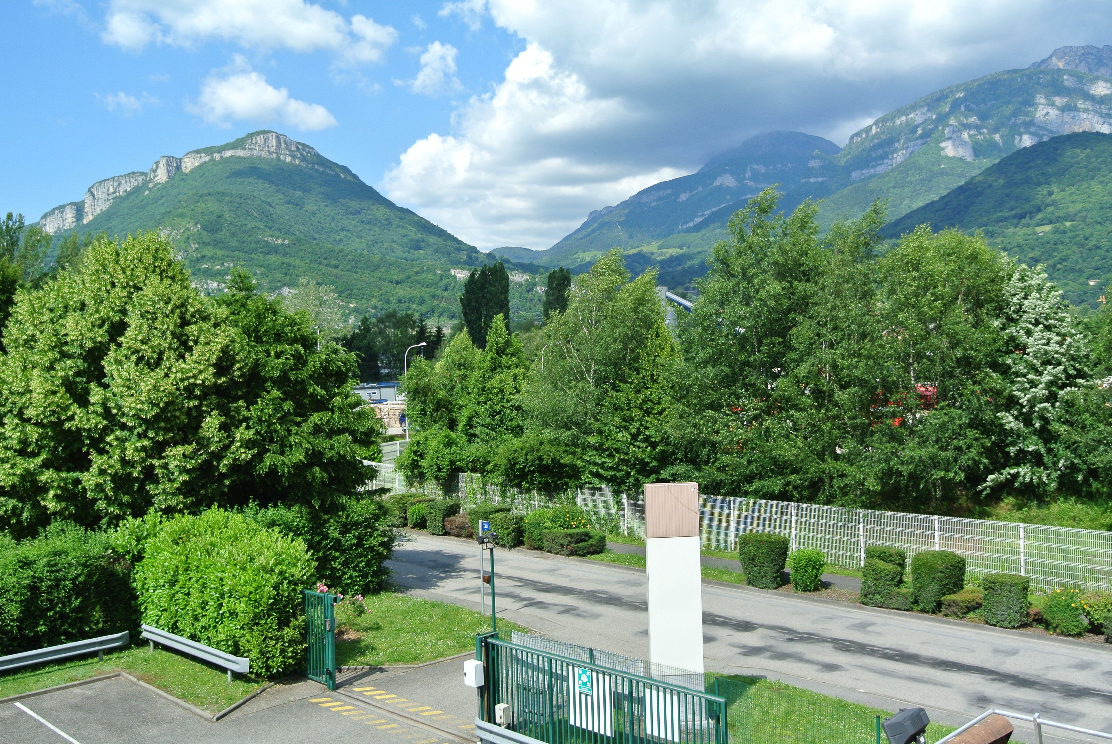 A parking area with a green fence, a bench, and a road leading to a mountainous landscape.