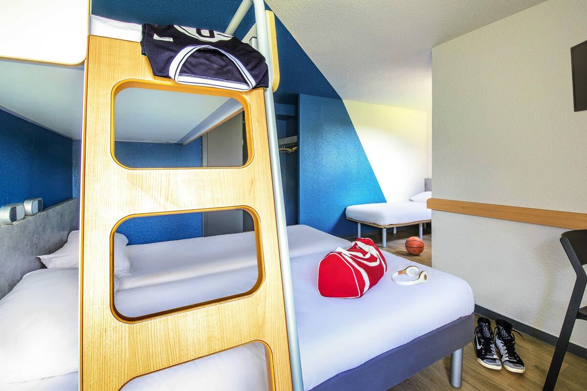 Ein Etagenbett mit Holzleiter, ein Einzelbett mit roter Tasche, ein Basketball und ein Paar Turnschuhe.