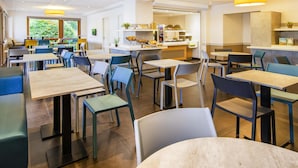 Un comedor moderno con mesas y sillas, una barra con alimentos y vistas al exterior con vegetación.