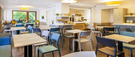 Un comedor moderno con mesas y sillas, una barra con alimentos y vistas al exterior con vegetación.