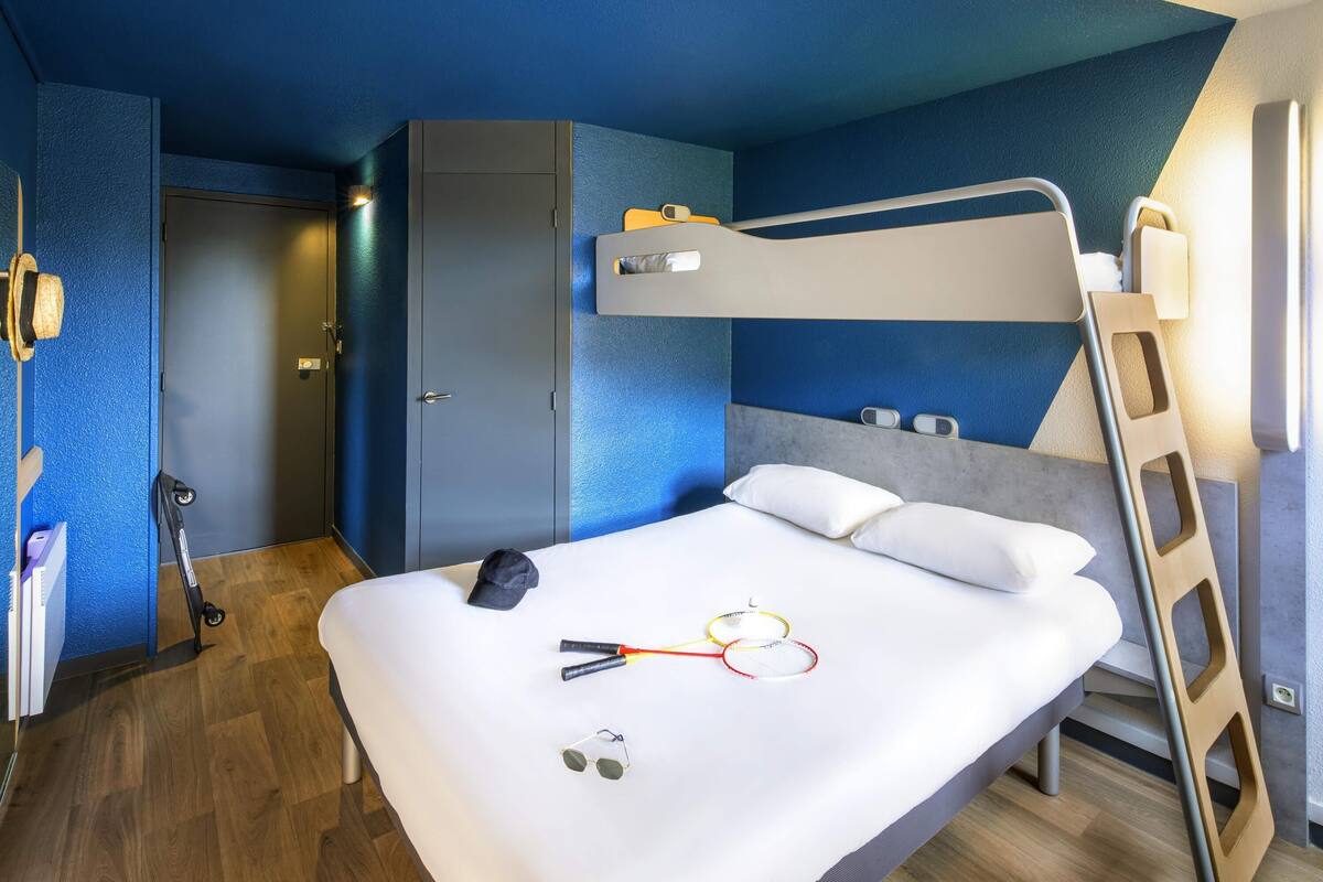 Ein Stockbett mit einer Stehle, ein Nachttisch, ein Schreibtisch und ein Kleiderschrank in einem Zimmer mit blauen Wänden und Holzboden.