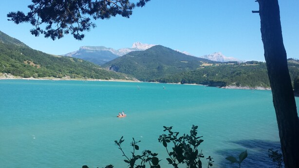 Un paisaje costero con aguas turquesas cristalinas, un barco a lo lejos y montañas al fondo.