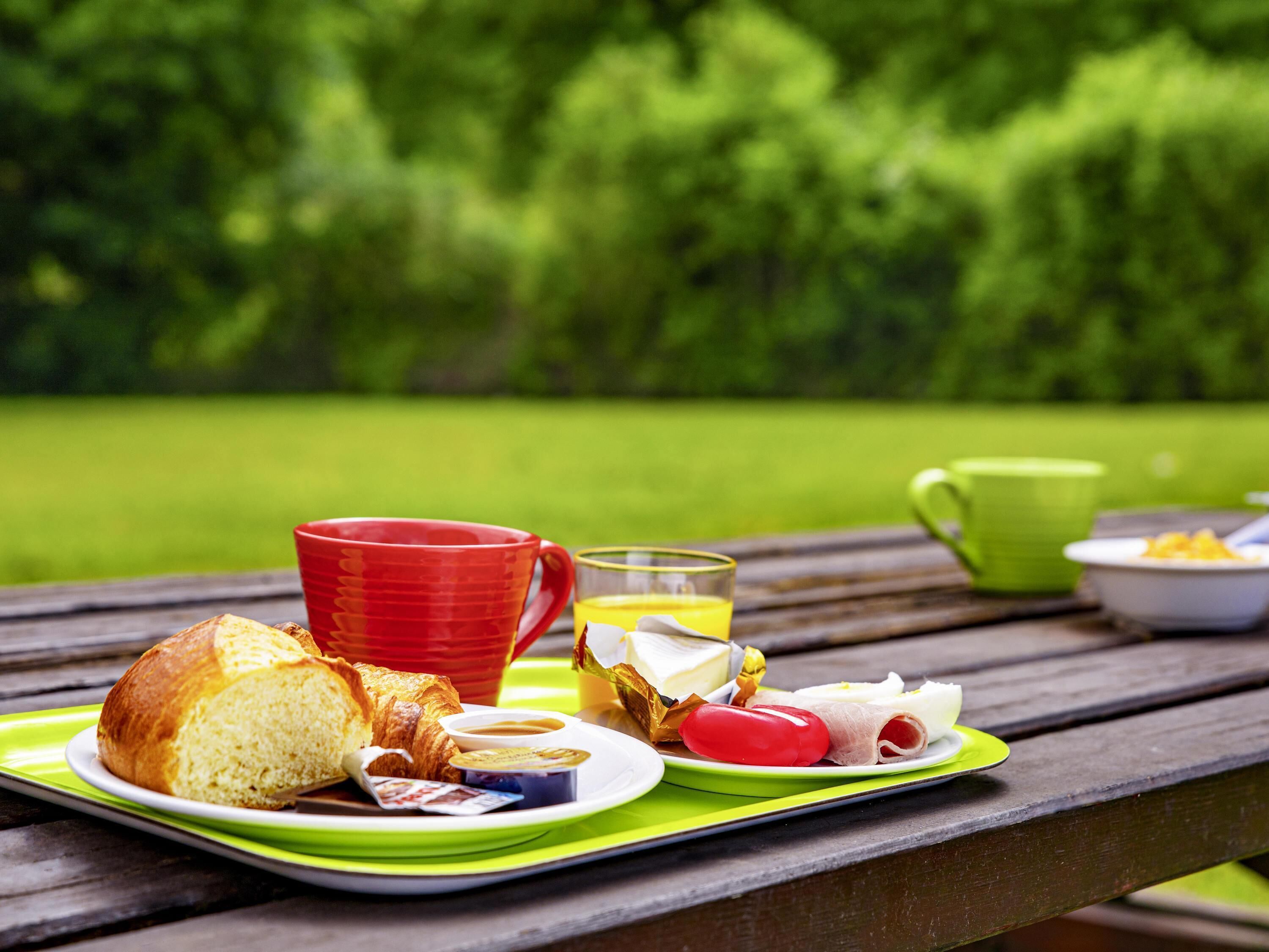 A picnic setup with food and drinks on a wooden table in a park.