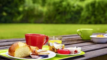 A picnic setup with food and drinks on a wooden table in a park.