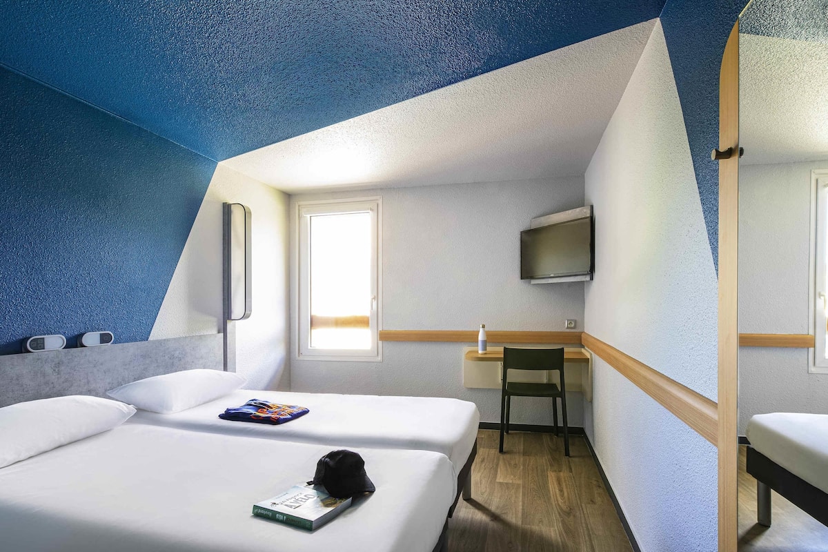 Ein Hotelzimmer mit Bett, Schreibtisch, Stuhl, Fernseher und Fenster.