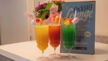 Trois cocktails décorés de fruits sont posés sur une table, un panneau indiquant l’entrée d’un bar à cocktails, et un bouquet de fleurs se trouve à l’arrière-plan.