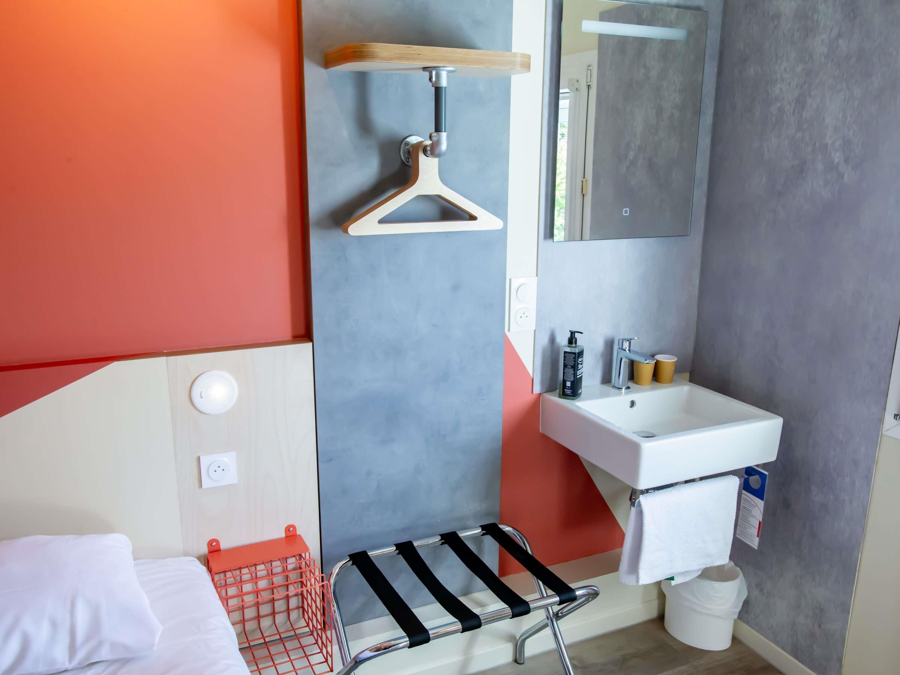 Un baño moderno con un lavamanos blanco, espejo y paredes anaranjadas.