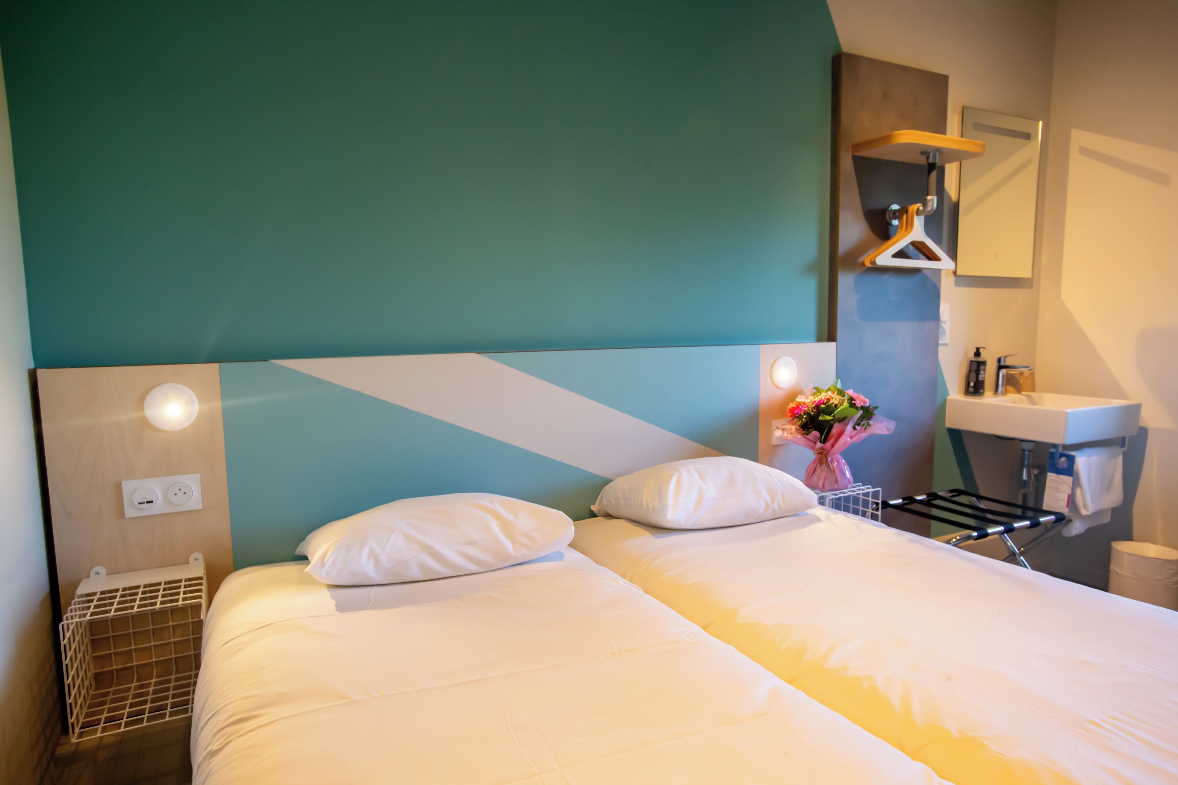 Habitación de hotel con dos camas, baño con lavamanos y espejo, y un tendedero de pared.