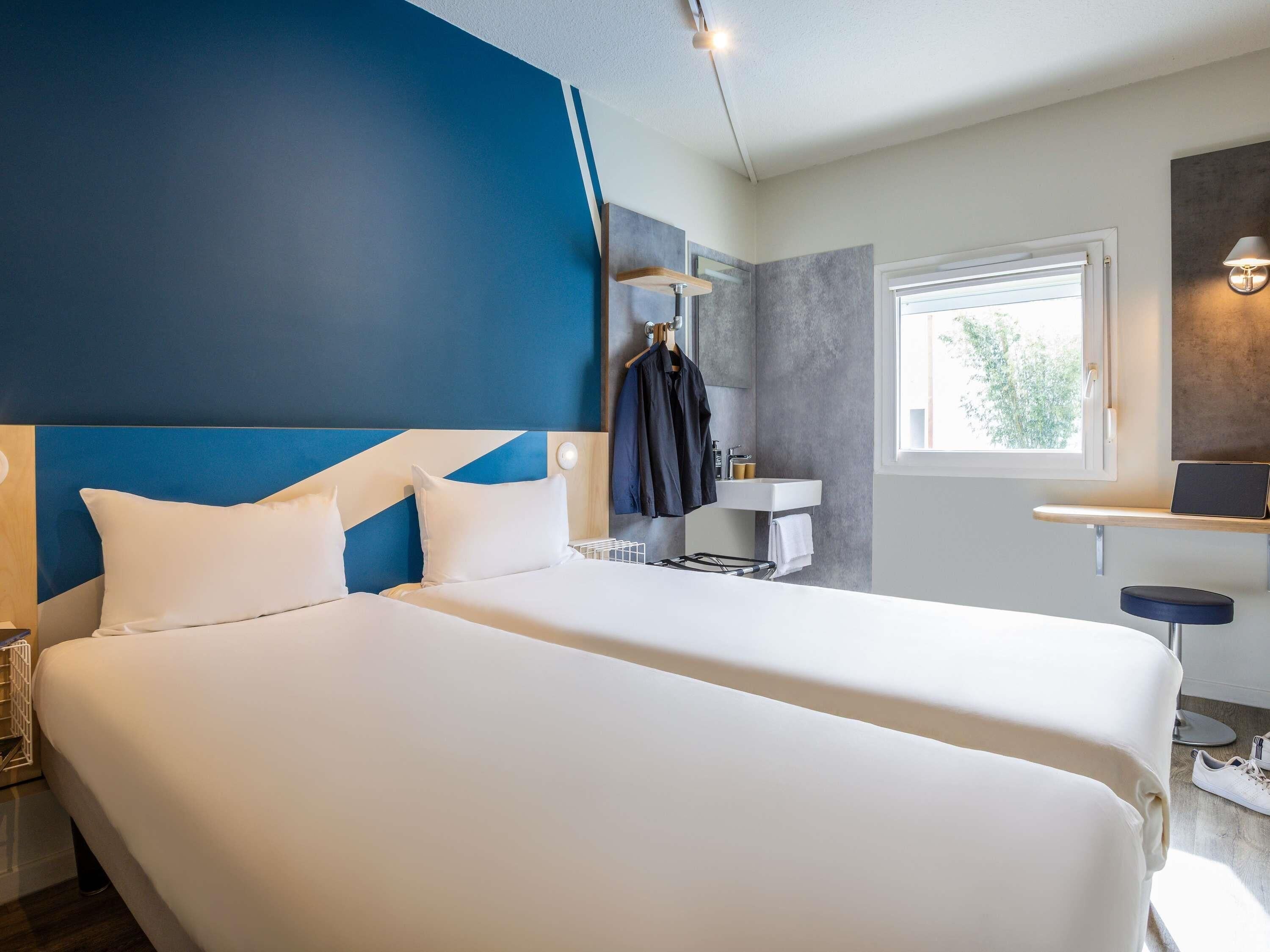 A hotel room with two beds, a bathroom, and a window.