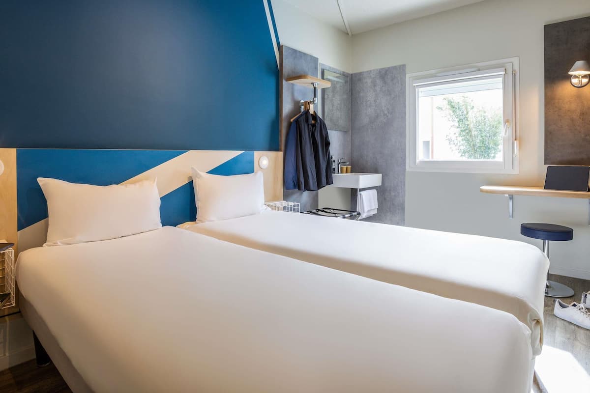 Een hotelkamer met twee bedden, een badkamer en een raam.