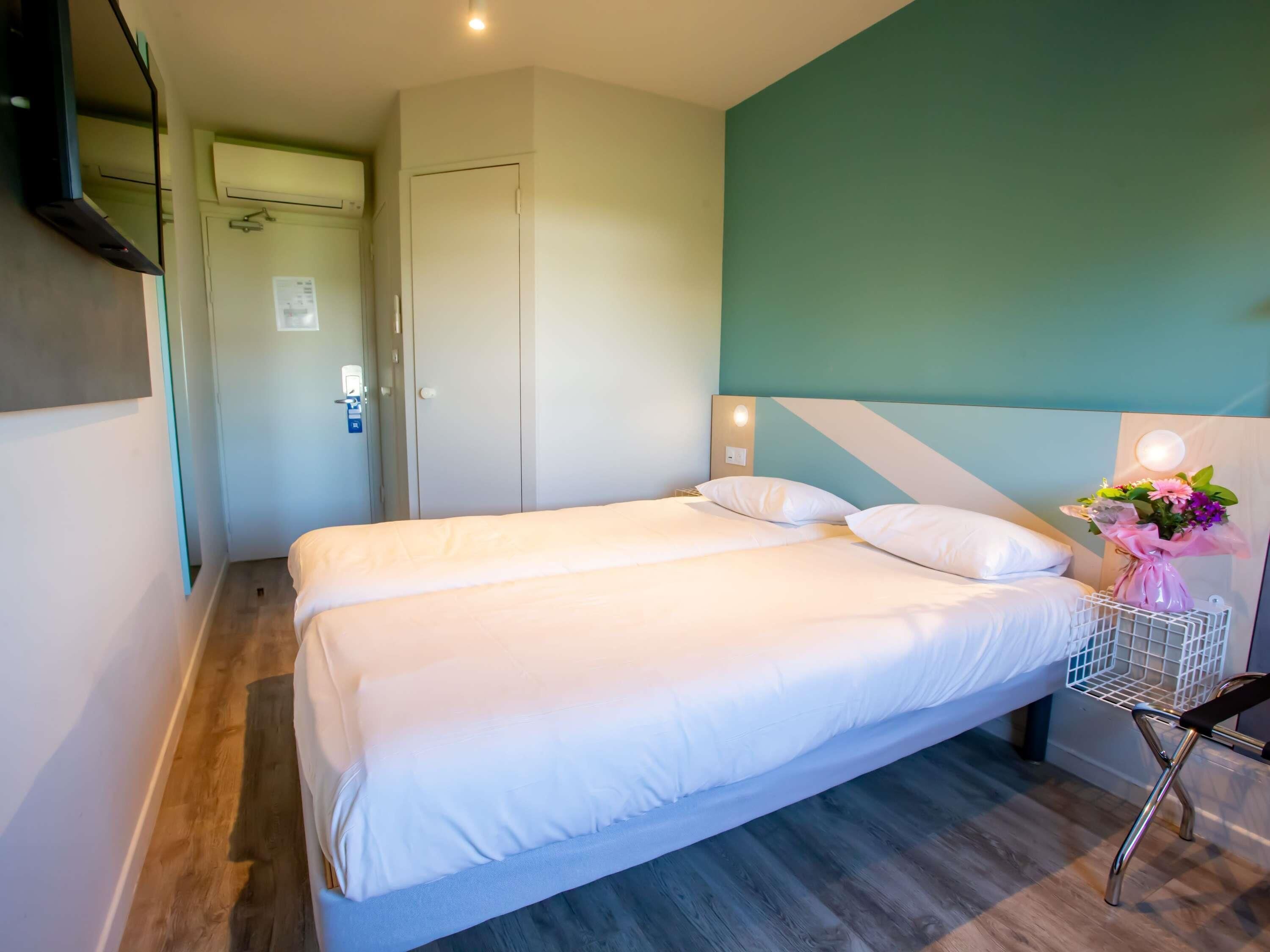 A double bed with white linens in a room with teal walls and a wooden floor.