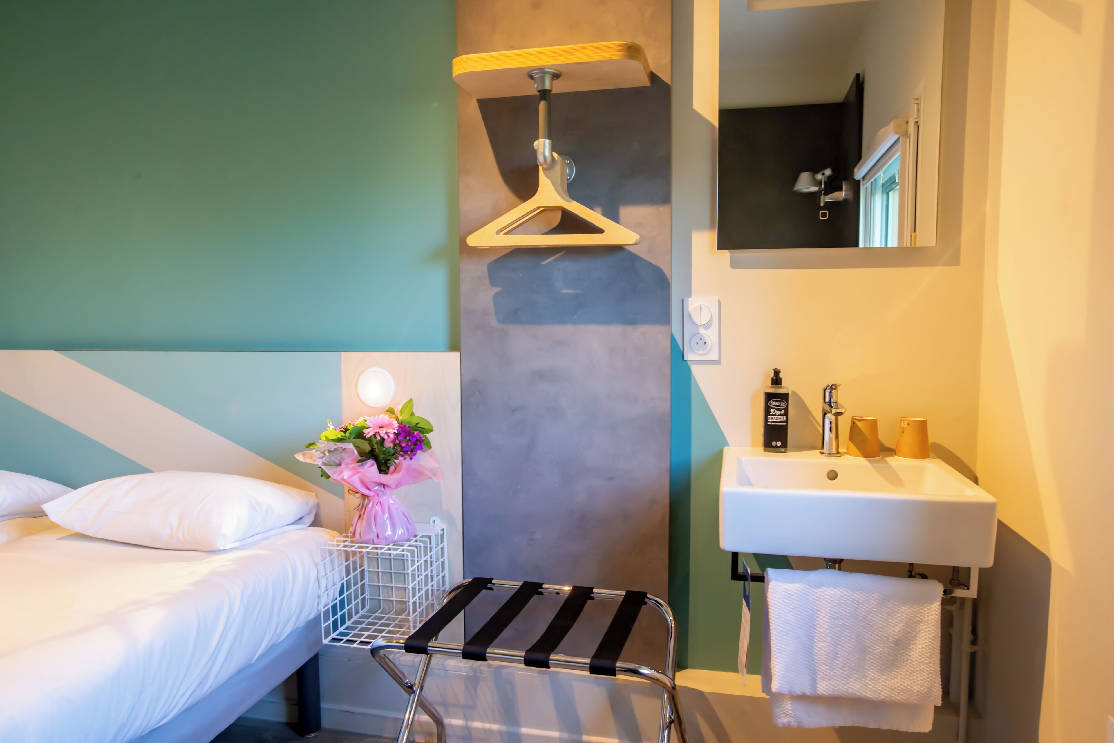 A hotel room with a bed, a small table, a hanging garment rack, a sink, and a mirror.