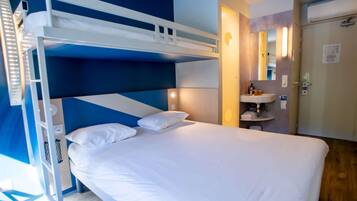 Una cama individual con ropa de cama blanca, una mesita de noche pequeña y un espejo sobre el lavabo en una habitación con paredes azules y beige.