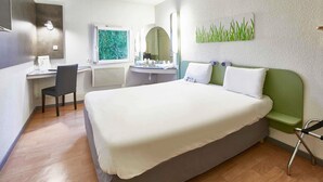 Habitación de hotel con cama, escritorio, silla y ventana con vistas a zonas verdes.