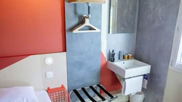 Un baño moderno con cama, ducha colgante, lavamanos y espejo.