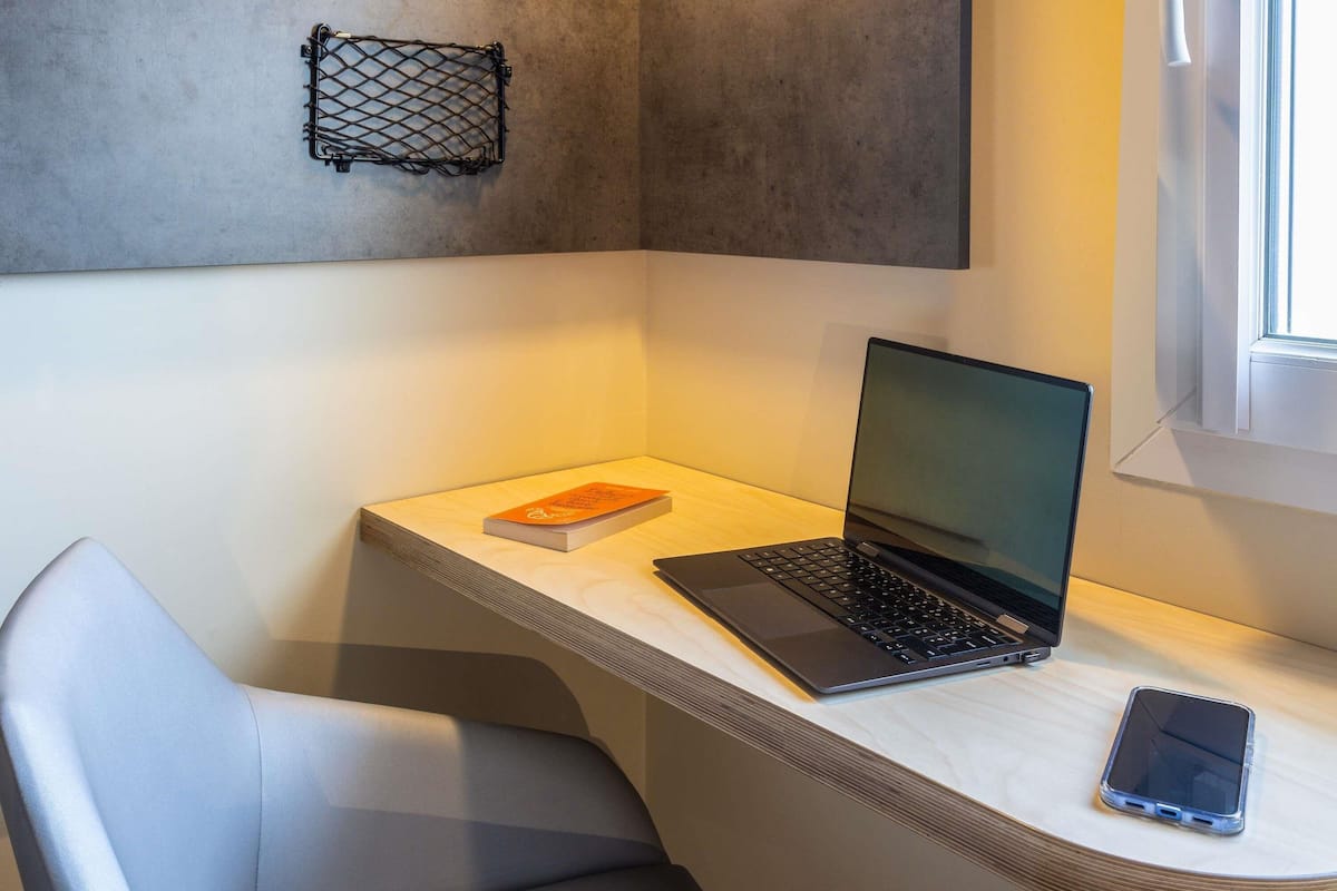 En bärbar dator står på ett skrivbord, bredvid den ligger en bok och en smartphone.