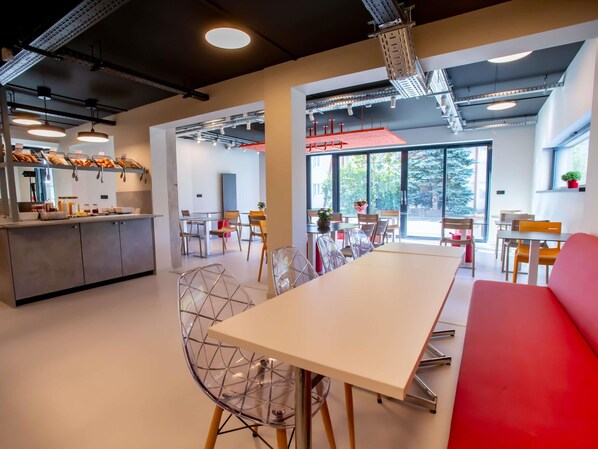 A modern dining area with a long table, chairs, and a red bench. - ibis budget Haguenau (Haguenau)