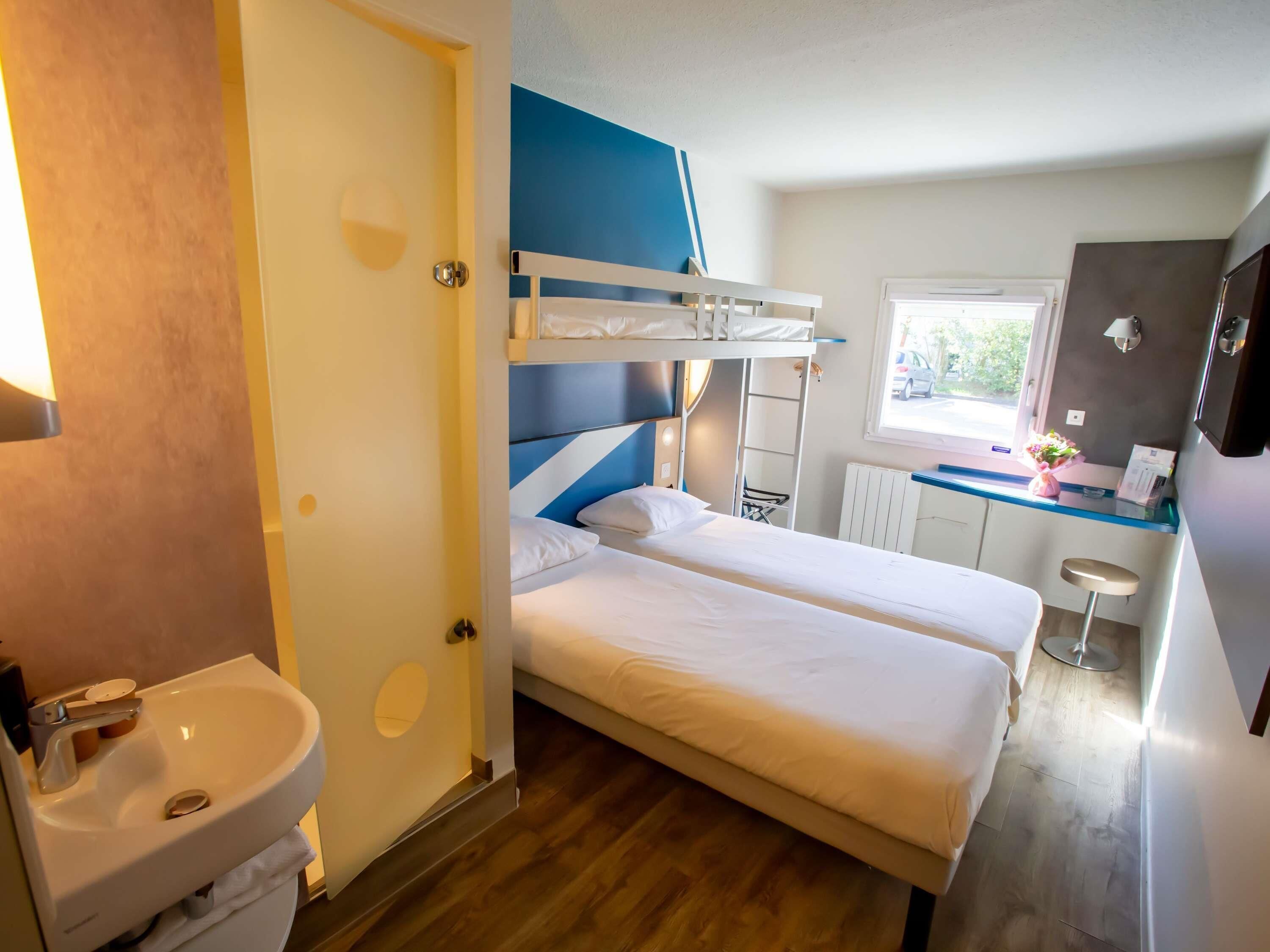 Een hotelkamer met een stapelbed, een wastafel, een klein raam en een kitchenette.