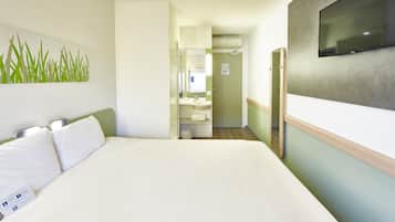 A hotel room with a large bed, a TV, a bathroom with a sink and mirror, and a green wall.