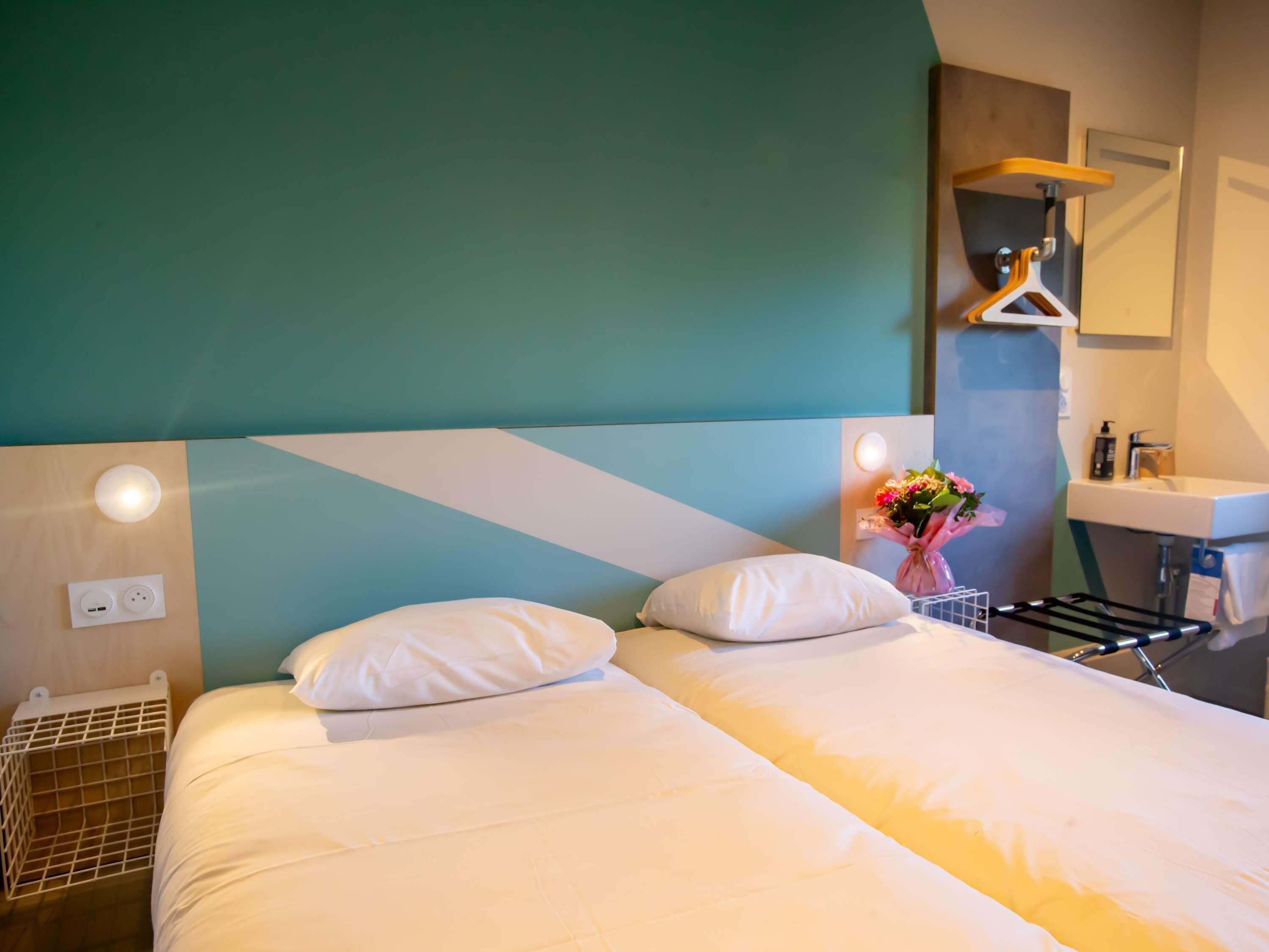 A hotel room with a bed, bedside table, wall-mounted light, and a bathroom with a sink and mirror.