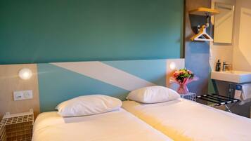 A hotel room with a bed, bedside table, wall-mounted light, and a bathroom with a sink and mirror.