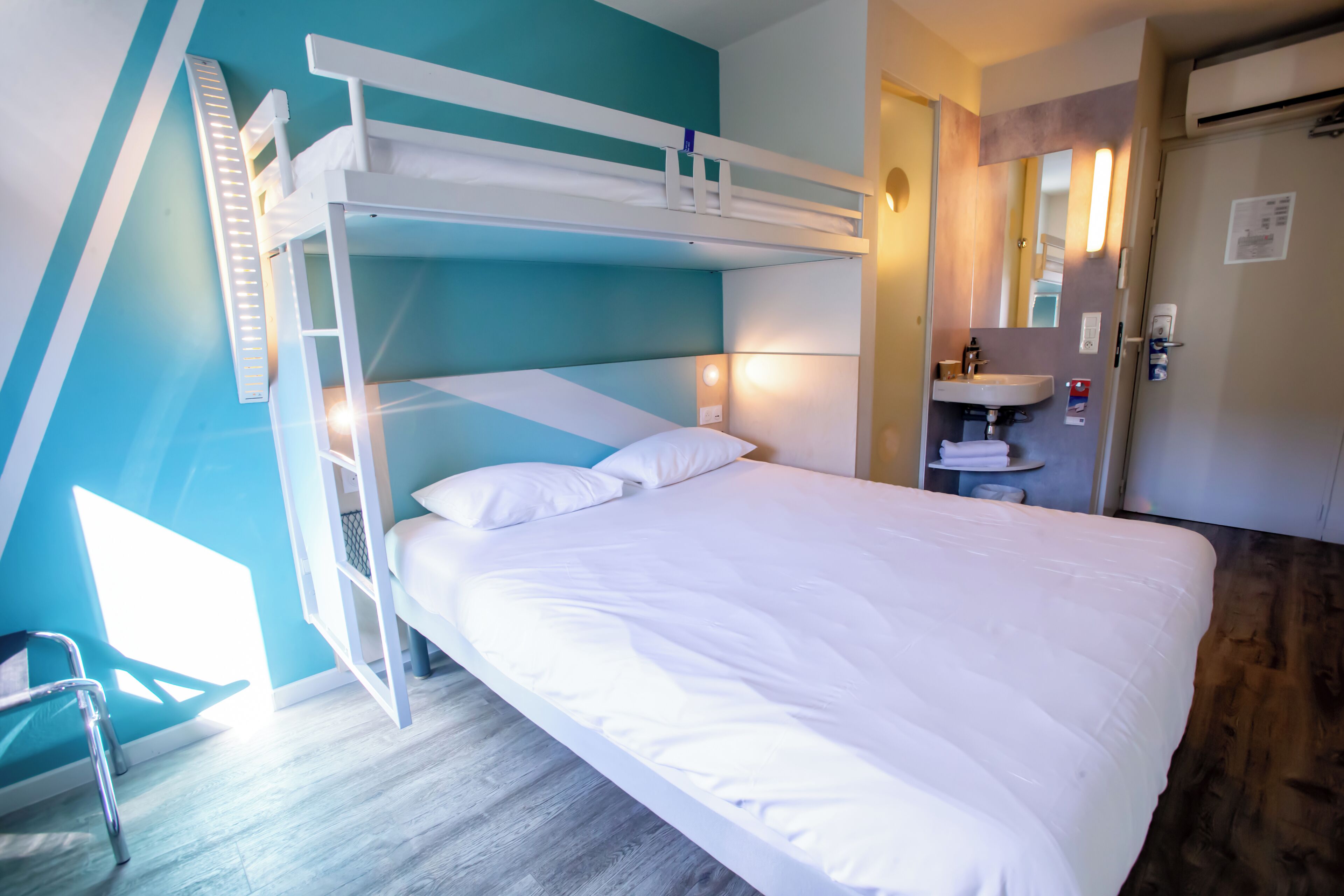 A bunk bed with white bedding, a bedside table, and a mirror.