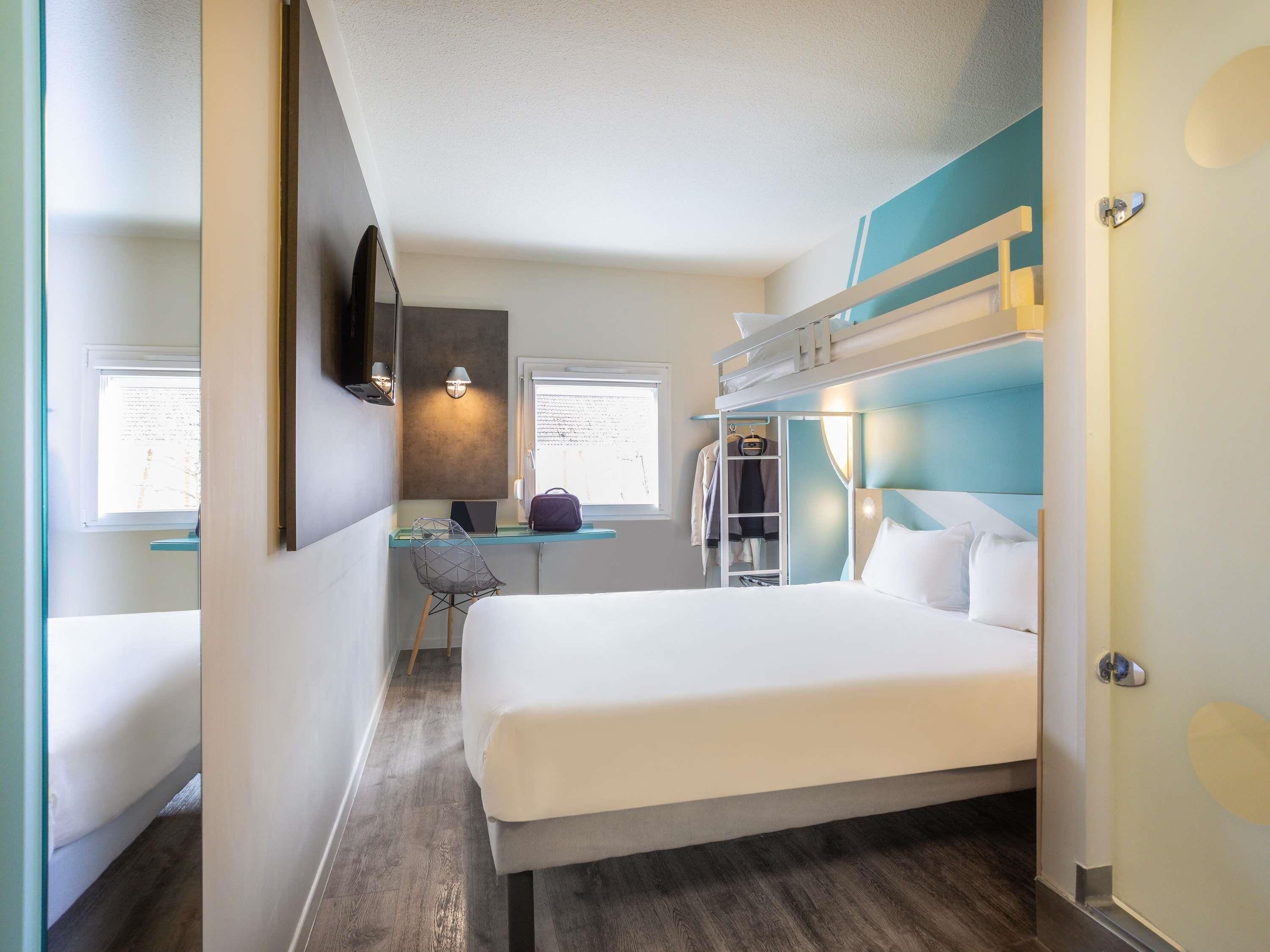 A hotel room with a bunk bed, a desk with a chair, a laptop, and a wardrobe.