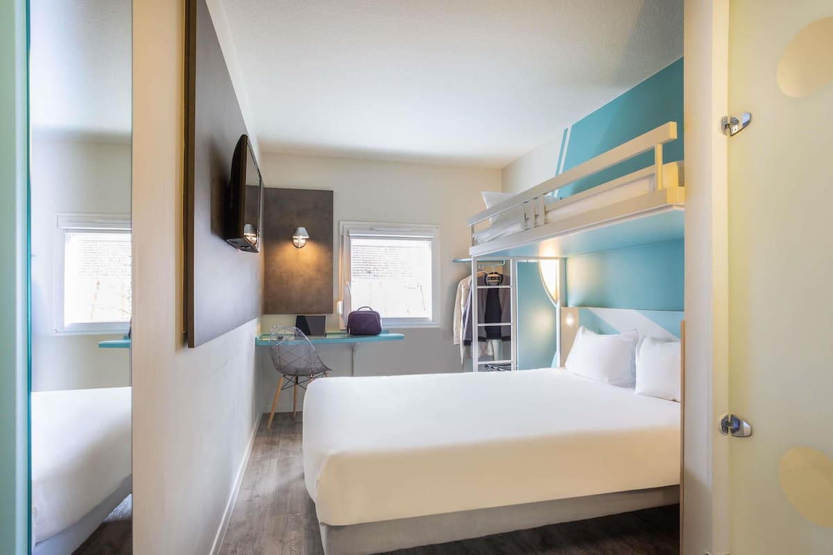 Een hotelkamer met een stapelbed, een bureau met een stoel, een laptop en een kledingkast.