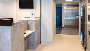 Un área de recepción moderna con un televisor de pantalla plana, un mostrador de recepción y un quiosco digital.