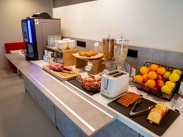 Una barra de desayuno con cafetera, tostadora, máquina para hacer gofres y una cesta de frutas.