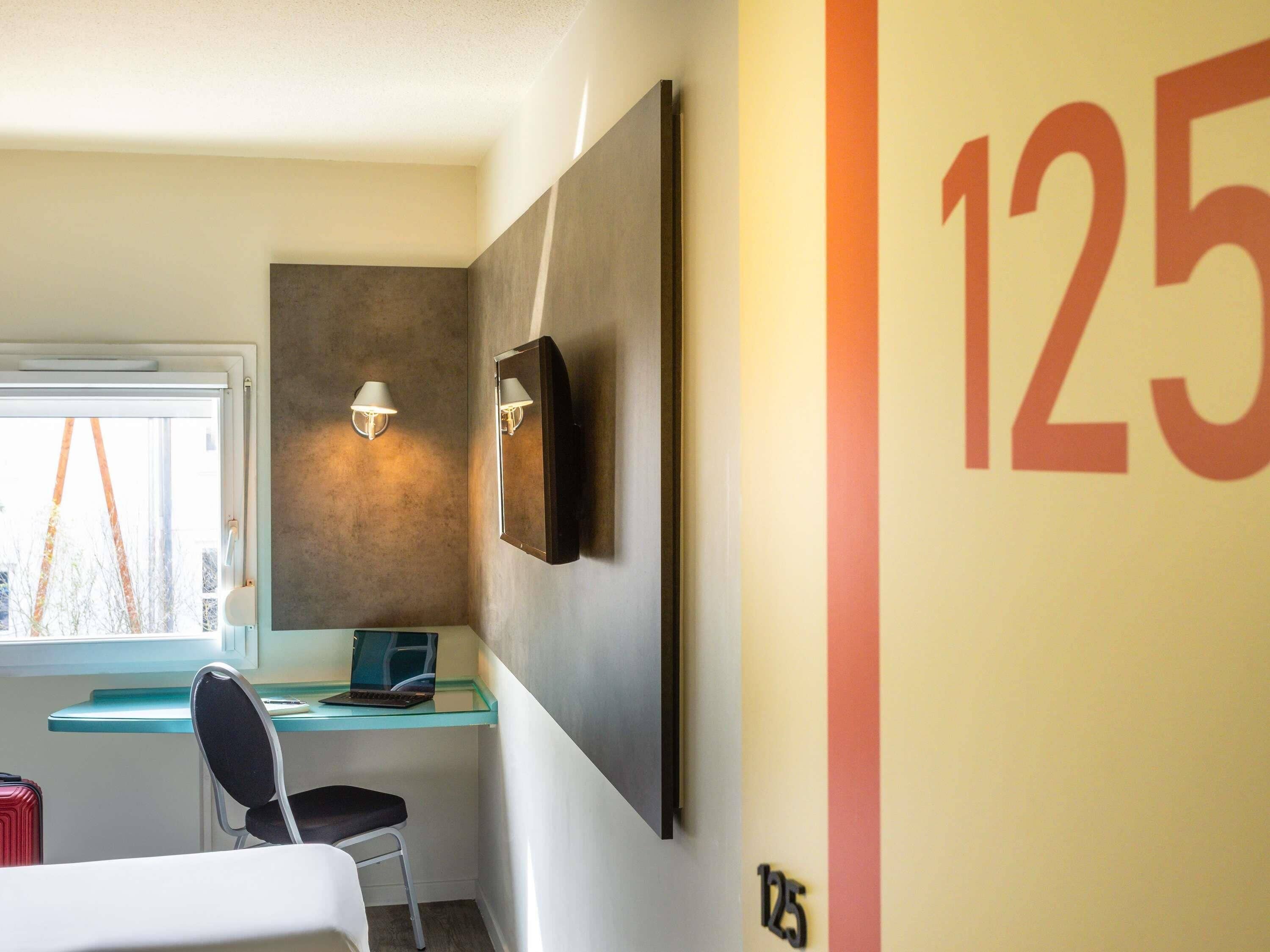 Ett hotellrum med ett skrivbord, en stol, en bärbar dator och ett stort nummer, ”125”, på väggen.