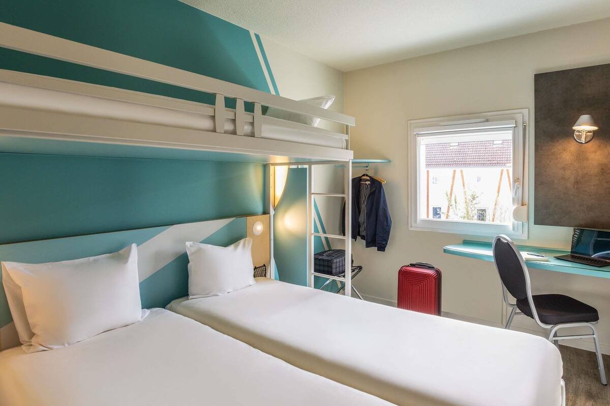 Ein Hotelzimmer mit Etagenbett, Schreibtisch, Computer, Stuhl und Koffer.