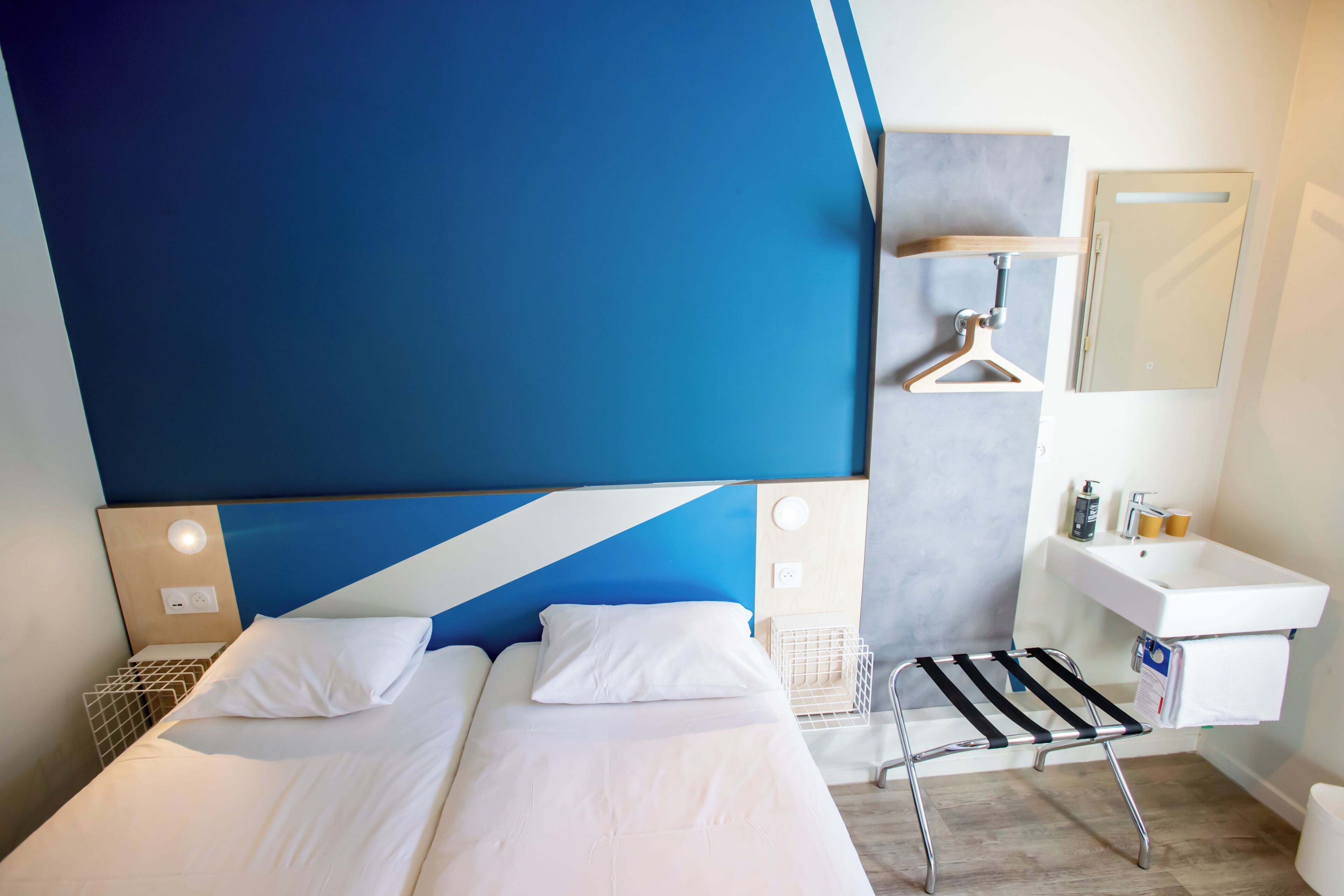 A hotel room with two beds, a bathroom with a sink and mirror, and a small seating area.
