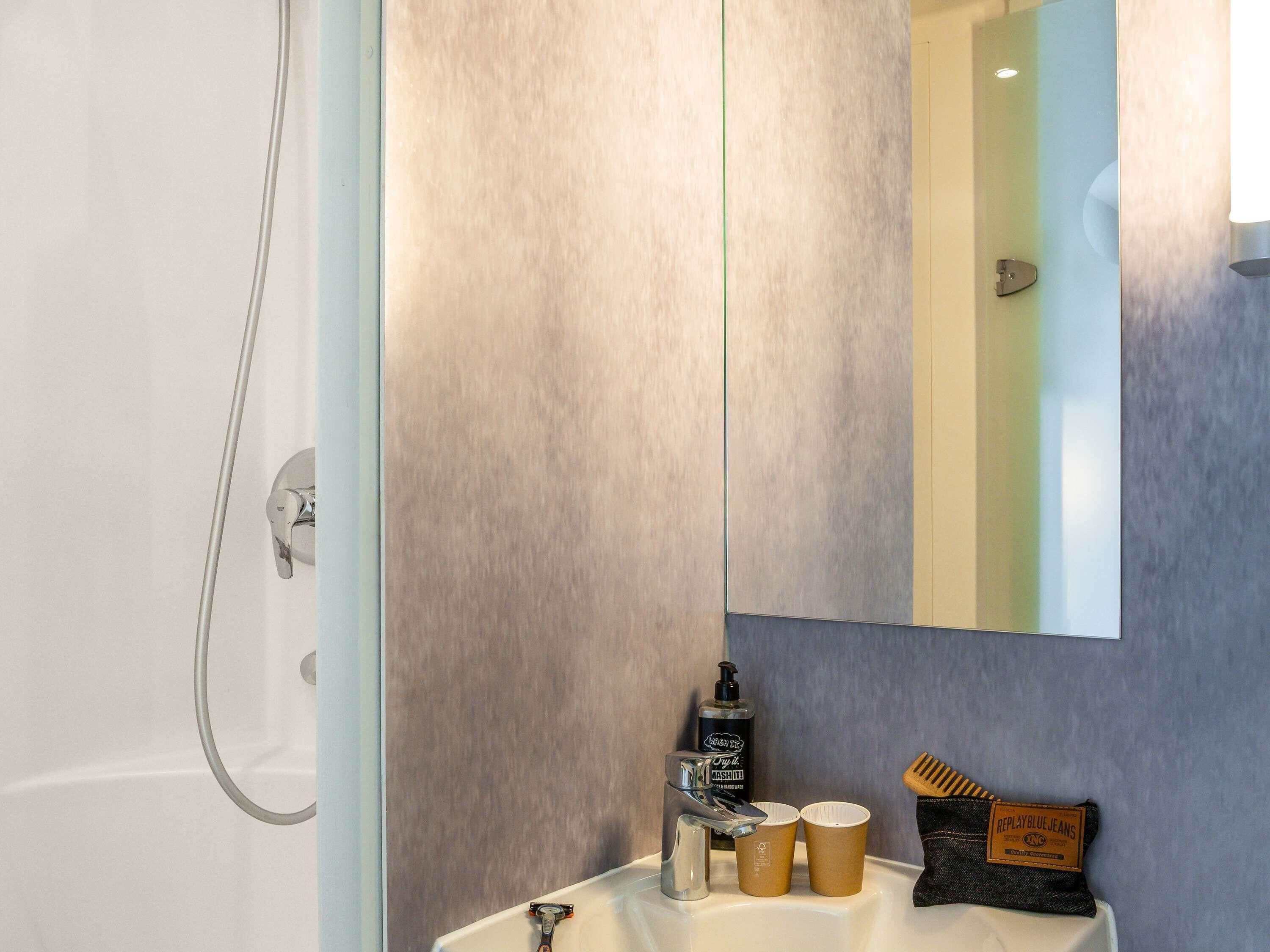 A bathroom with a shower, a sink, a mirror, and toiletries.