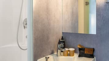 A bathroom with a shower, a sink, a mirror, and toiletries.