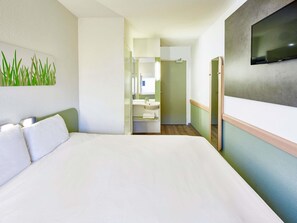 Ein Hotelzimmer mit einem großen Bett, einem wandmontierten Flachbildfernseher, einem Badezimmer mit Waschbecken und Spiegel sowie einem Flur, der in ein weiteres Zimmer führt.