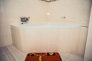 A corner bathroom with a bathtub, a shower, and a towel rack. - Matilinda Lodge (Bulawayo)