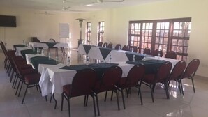 A conference room with multiple tables and chairs, equipped with water bottles and a projector screen. - Matilinda Lodge (Bulawayo)