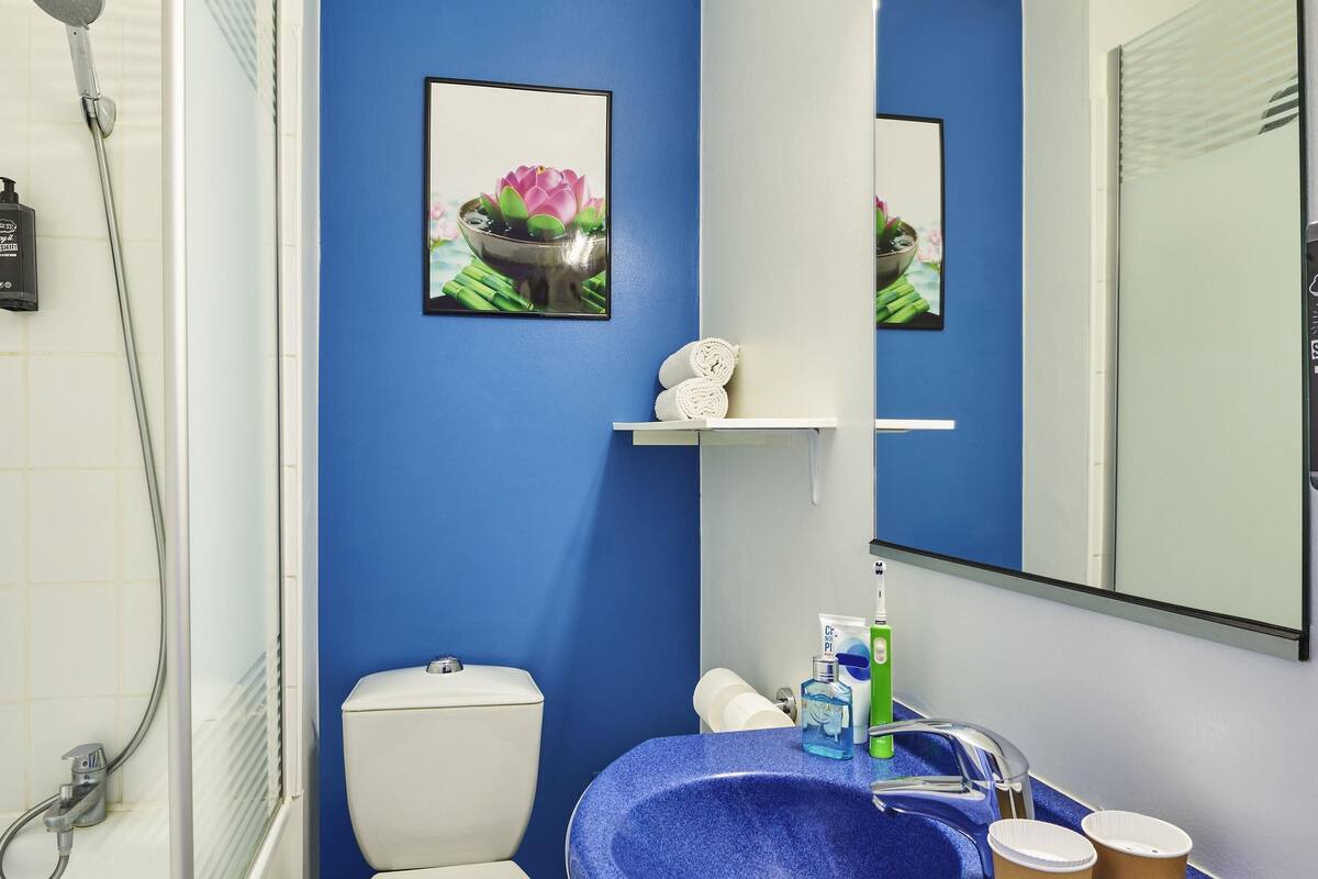 A bathroom with a blue sink, a toilet, a shower, and a mirror.