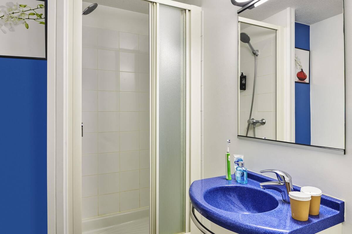 A bathroom with a shower, a sink with a blue countertop, and a mirror above the sink.