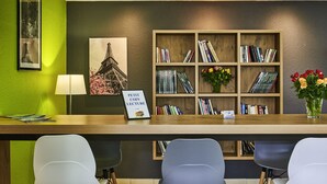 Una mesa de recepción con una estantería de madera, un cuadro con la Torre Eiffel, un cartel que dice “PETIT COIN LECTURE” y un florero con flores.
