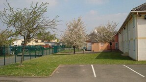 A parking lot with a building on the right, a fenced area with trees, and a clear sky.