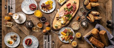 A wooden table with various breakfast items including eggs, sausages, and pastries.