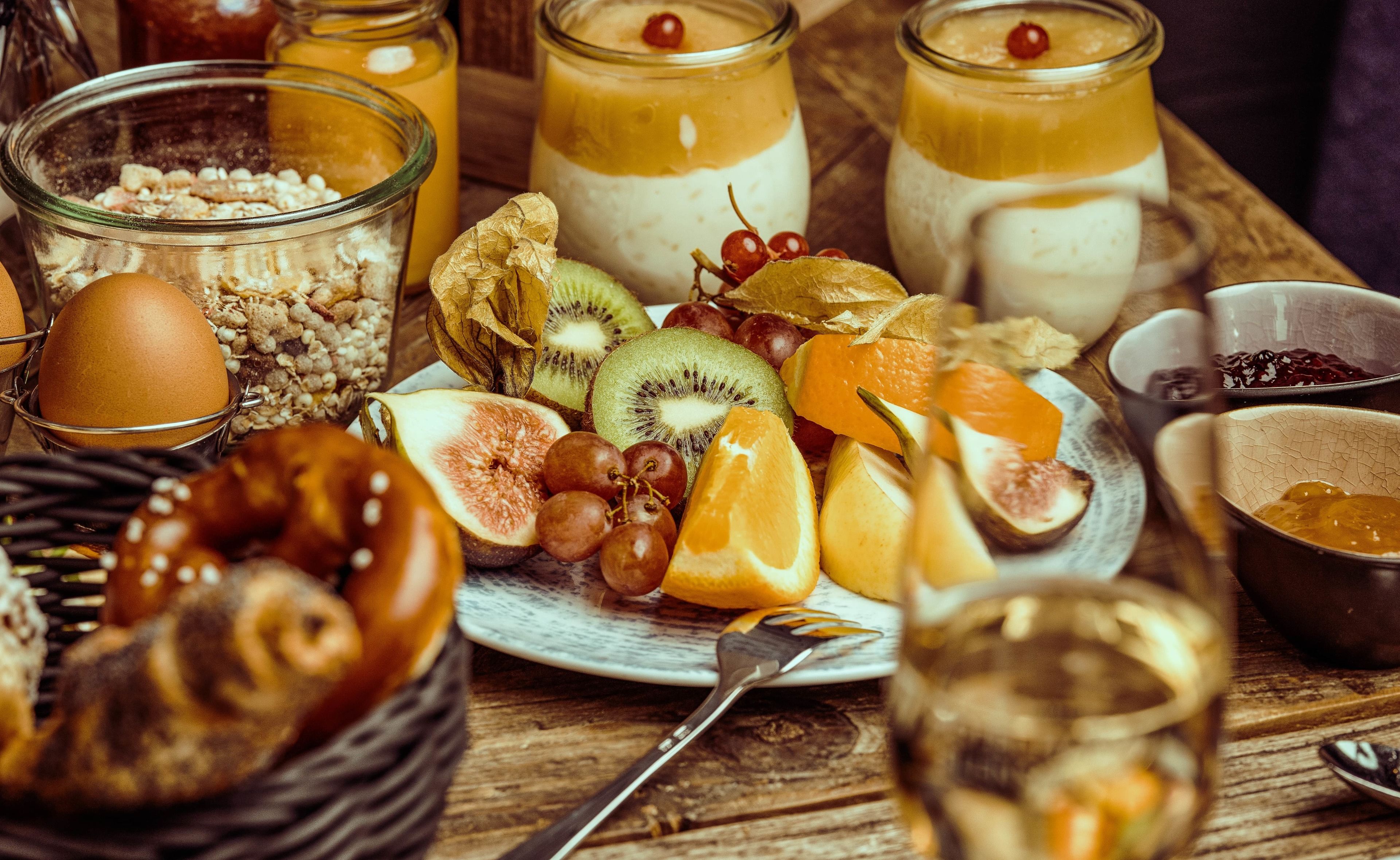 A breakfast setting with various fruits, eggs, and beverages on a wooden table.