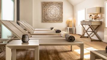 Relax in a serene spa room with a minimalist design, featuring a series of loungers, a tapestry, and a cozy reading area.